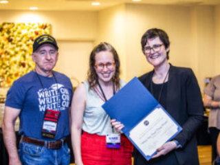 SFWA CFO Jonathan P. Brazee (left) and SFWA President (Kate Ristau) celebrate Nebula Finalist Aimee Ogden. (Photo Credit: Kaitrin Acuna, 2025.)