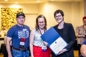 SFWA CFO Jonathan P. Brazee (left) and SFWA President (Kate Ristau) celebrate Nebula Finalist Aimee Ogden. (Photo Credit: Kaitrin Acuna, 2025.)