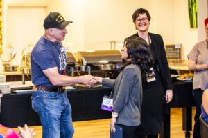 SFWA CFO Jonathan P. Brazee shakes hands with Nebula Award Winner A. W. Prihandita while SFWA President Kate Ristau smiles on. (Photo Credit: Kaitrin Acuna, 2025.)