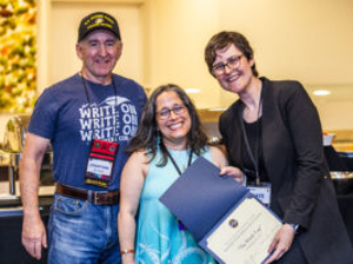 SFWA CFO Jonathan P. Brazee (left) and SFWA President (Kate Ristau) celebrate Nebula Finalist Jennifer Hudak. (Photo Credit: Kaitrin Acuna, 2025.)