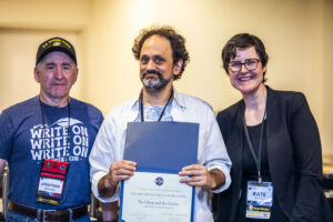 SFWA CFO Jonathan P. Brazee (left) and SFWA President (Kate Ristau) celebrate Nebula Finalist Benjamin Rosenbaum. (Photo Credit: Kaitrin Acuna, 2025.)