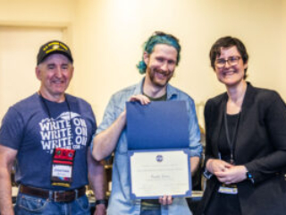 SFWA CFO Jonathan P. Brazee (left) and SFWA President (Kate Ristau) celebrate Nebula Finalist Paul Dean. (Photo Credit: Kaitrin Acuna, 2025.)
