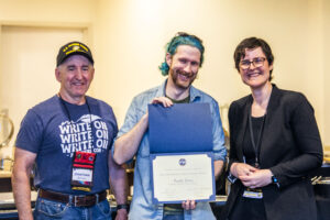 SFWA CFO Jonathan P. Brazee (left) and SFWA President (Kate Ristau) celebrate Nebula Finalist Paul Dean. (Photo Credit: Kaitrin Acuna, 2025.)