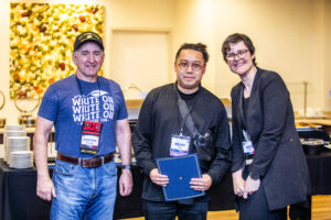 SFWA CFO Jonathan P. Brazee (left) and SFWA President (Kate Ristau) celebrate Nebula Finalist Remy Siu. (Photo Credit: Kaitrin Acuna, 2025.)
