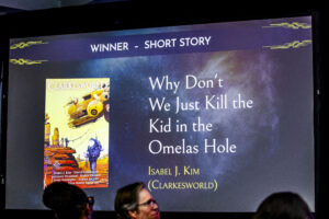 Display screen for part of the Nebula Awards Ceremony, featuring the winner for Best Short Story: &quot;Why Don&#039;t We Just Kill the Kid in the Omelas Hole&quot;, by Isabel J. Kim, at Clarkesworld. (Photo Credit: Kaitrin Acuna, 2025.)