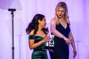 Nebula Award Winner A. W. Prihandita, carrying her Nebula Award off stage, escorted by Katelyn (Kat) Brehm. (Photo Credit: Kaitrin Acuna, 2025.)