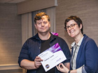 Nathan Lucas receives a certificate of appreciation from SFWA President Kate Ristau. (Photo Credit: Kaitrin Acuna, 2025.)