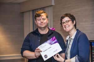 Nathan Lucas receives a certificate of appreciation from SFWA President Kate Ristau. (Photo Credit: Kaitrin Acuna, 2025.)
