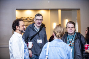 Hang time! Nebula Finalist Benjamin Rosenbaum, Jason Hill from Choice of Games, and fellow attendees mingle at our 60th Anniversary Nebula Awards Conference. (Photo Credit: Kaitrin Acuna, 2025.)